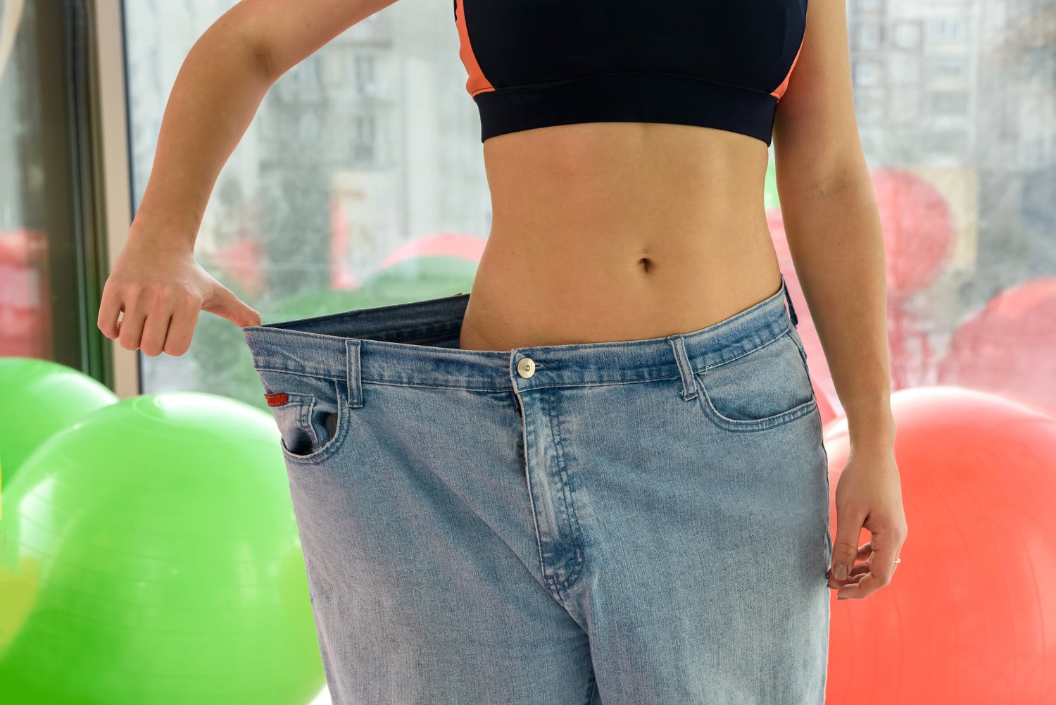 Egy fitneszteremben álló személy, aki bő ruháját mutatja fogyás után a Genheal Tirzepatide segítségével.